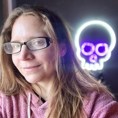 Author Sharon Clark (middle aged woman with nerd glasses) in front of a neon skull